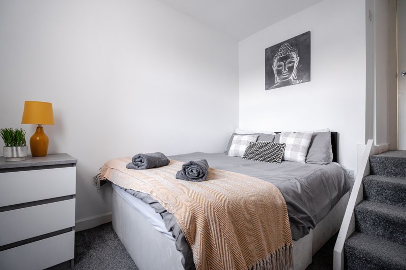 Modern bedroom with double bed, beige throw, gray pillows and wall-mounted artwork