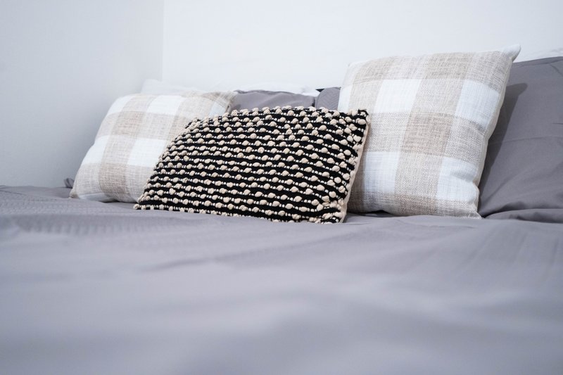 Bed with gray bedding, patterned throw blanket, and decorative plaid cushions