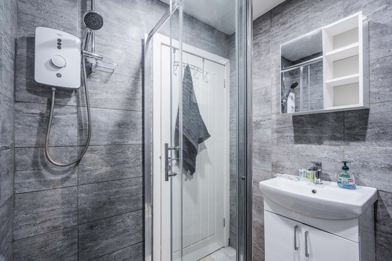 Modern bathroom with grey tile walls, shower enclosure, white sink vanity and mirror cabinet