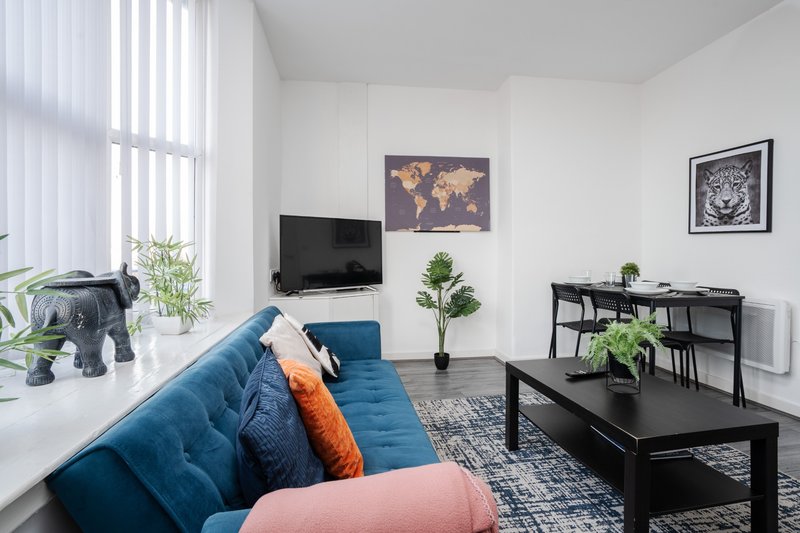 Modern living room with blue sofa, black coffee table, TV, desk and potted plants