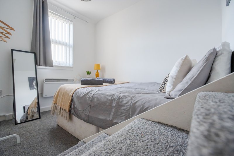 Modern bedroom with double bed, grey bedding, cushions, window with blinds and curtains