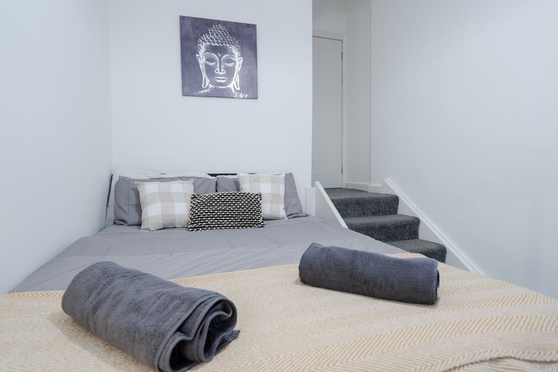 Minimalist bedroom with gray bed, rolled towels, decorative Buddha artwork, and neutral flooring