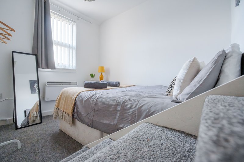 Modern bedroom with double bed, grey bedding, pillows, and carpet flooring