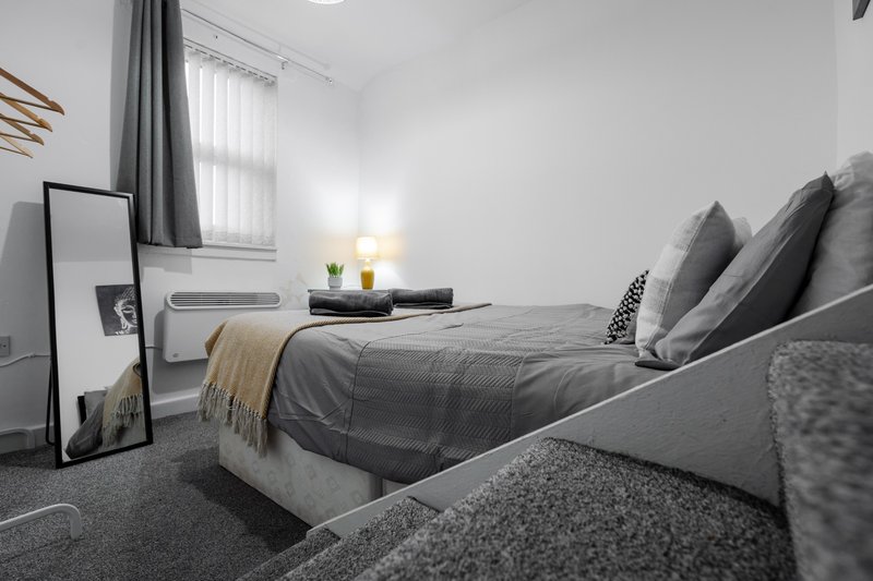 Modern bedroom with double bed, grey bedding, pillows, bedside lamp and window with curtains