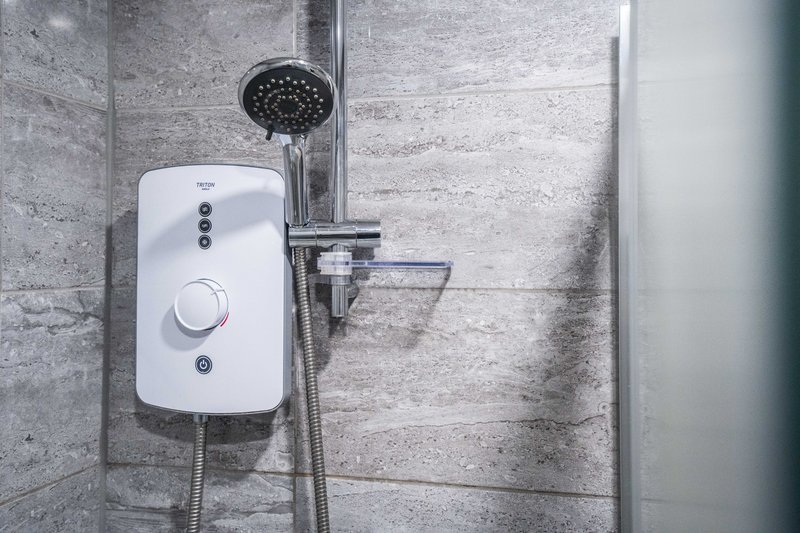 Bathroom shower with white instant water heater, black showerhead and grey tile walls
