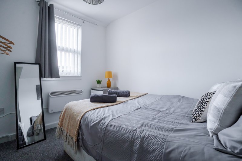 Bright bedroom with double bed, grey bedding, mirror, window with grey curtains
