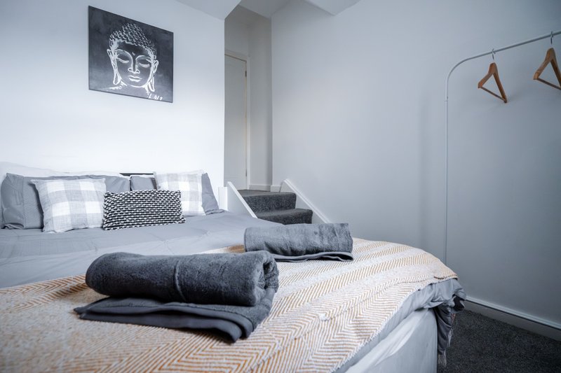 Modern bedroom with two beds, rolled towels, cushions, and framed artwork on wall