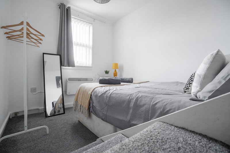 Modern bedroom with grey bed, pillows, wooden coat stand, and window with grey curtains