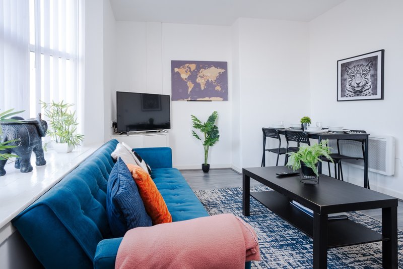 Modern living room with blue sofa, pink cushion, black coffee table and shelving unit