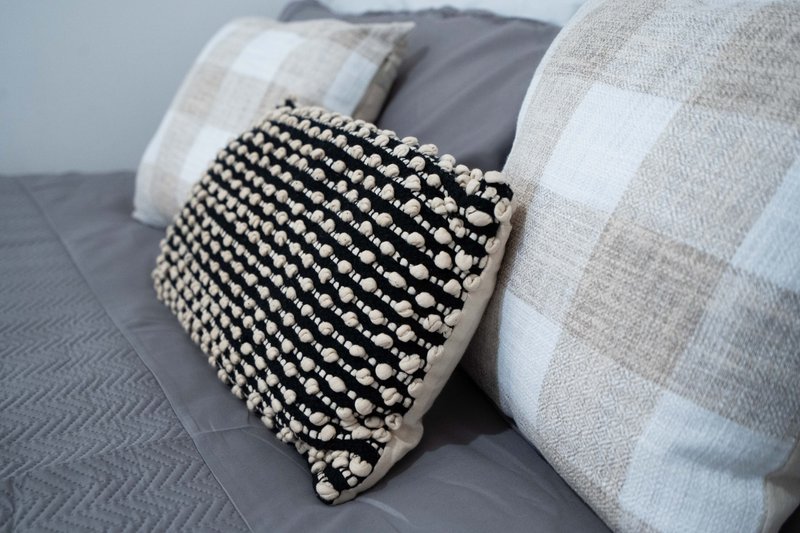 Bed with grey duvet, patterned cushions and black and white decorative pillow