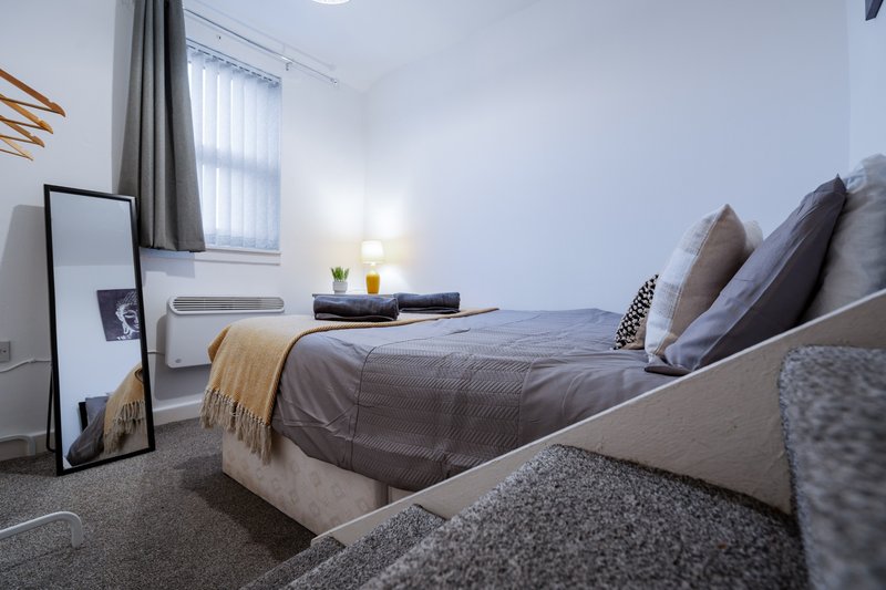 Modern bedroom with double bed, grey bedding, pillows, and warm throw blanket