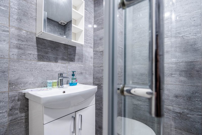 Modern bathroom with grey tile walls, white sink vanity, mirror cabinet and shower enclosure