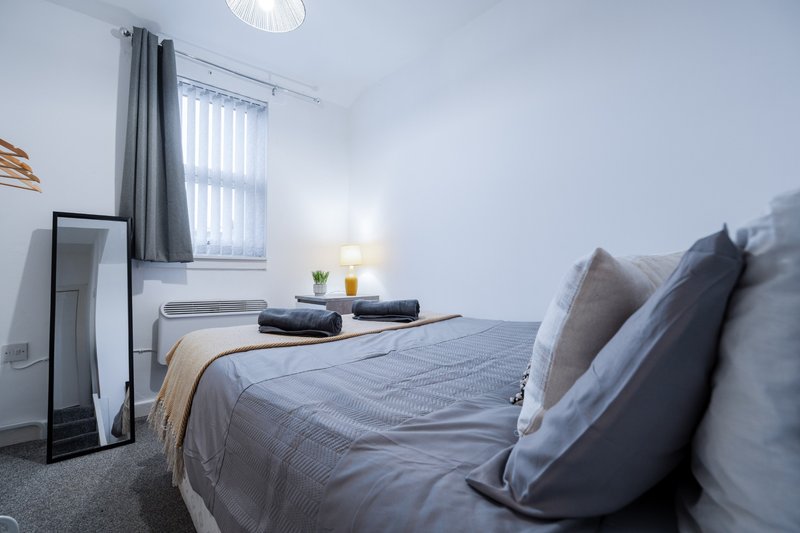 Modern bedroom with double bed, grey bedding, pillows, bedside lamp and vertical blinds
