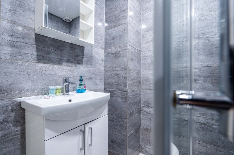 Modern bathroom with gray tile walls, white sink vanity, mirror and toiletries