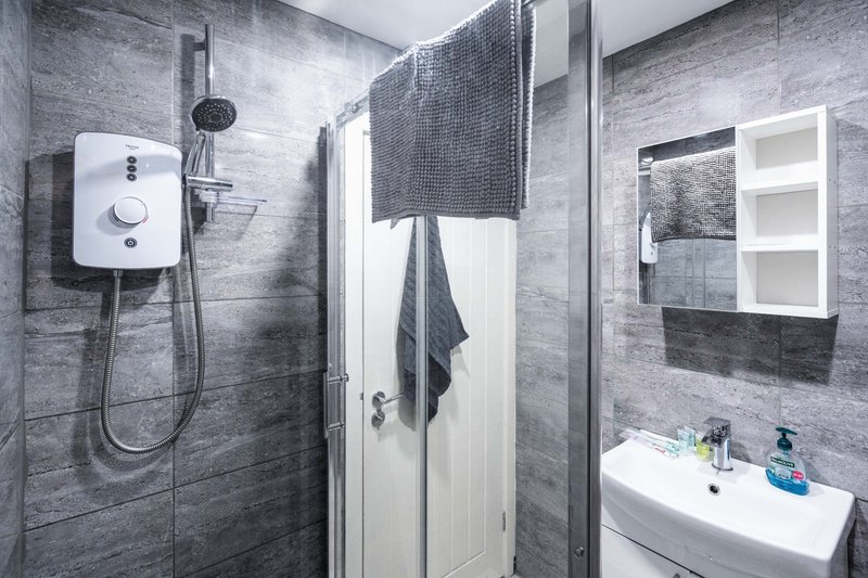 Modern bathroom with grey tile walls, shower enclosure, wall-mounted sink and mirror cabinet