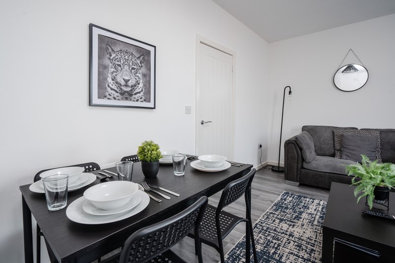 Modern dining area with black table, place settings, grey sofa and wall art