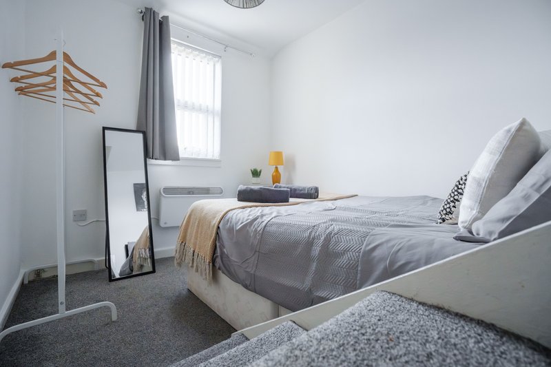 Bright bedroom with double bed, grey bedding, wooden clothes rack and window