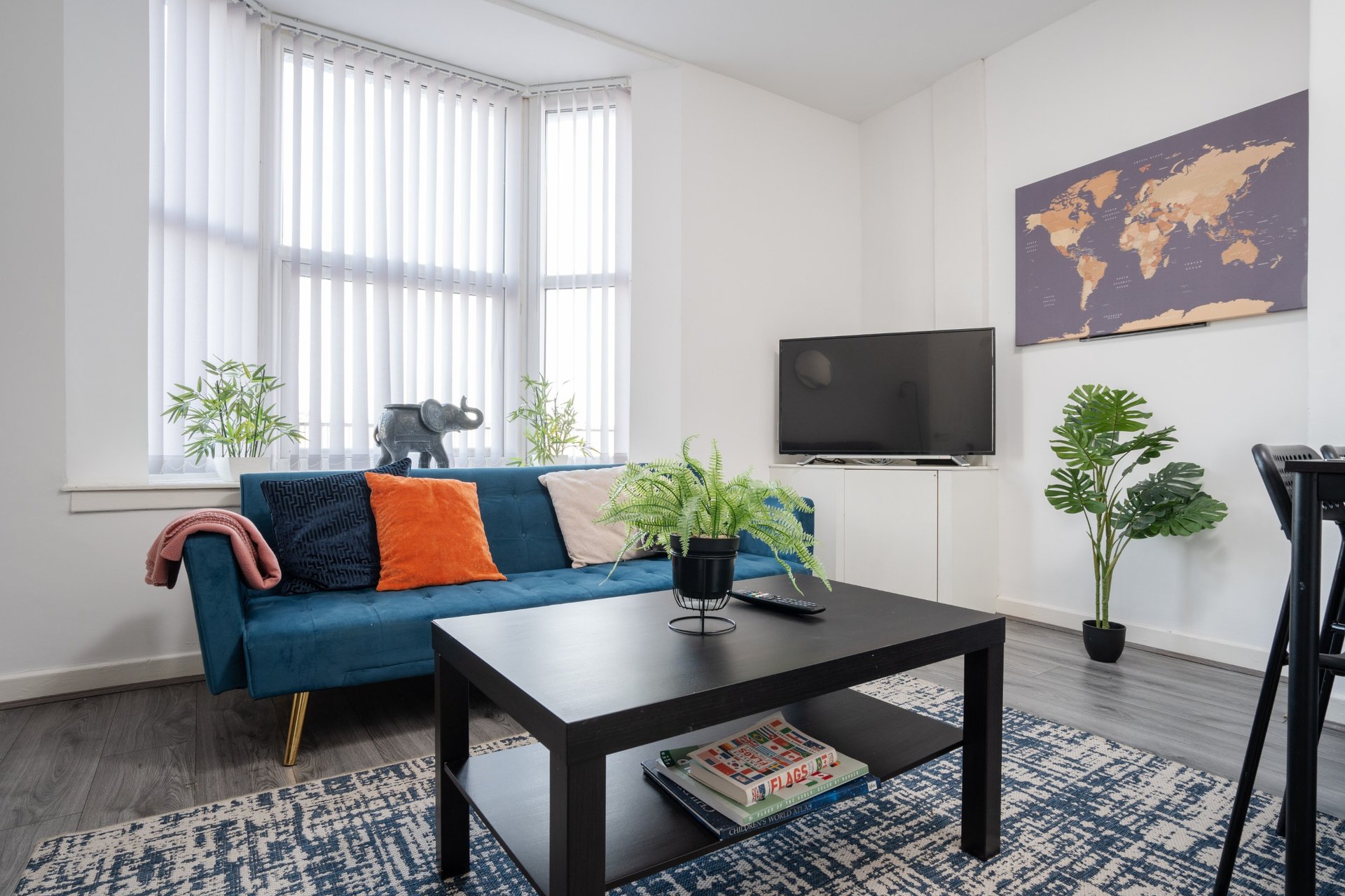 Modern living room with blue sofa, black coffee table, TV, potted plants and world map artwork