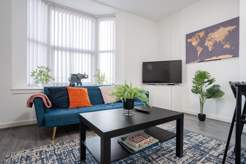 Modern living room with blue sofa, black coffee table, TV, potted plants and world map artwork