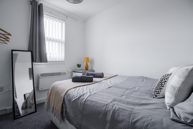 Modern bedroom with double bed, grey bedding, window with curtains, and minimal decor
