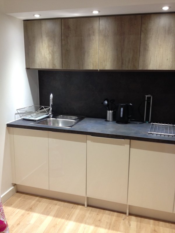 Modern kitchenette with cream and wood cabinetry, black countertop and backsplash, stainless steel sink