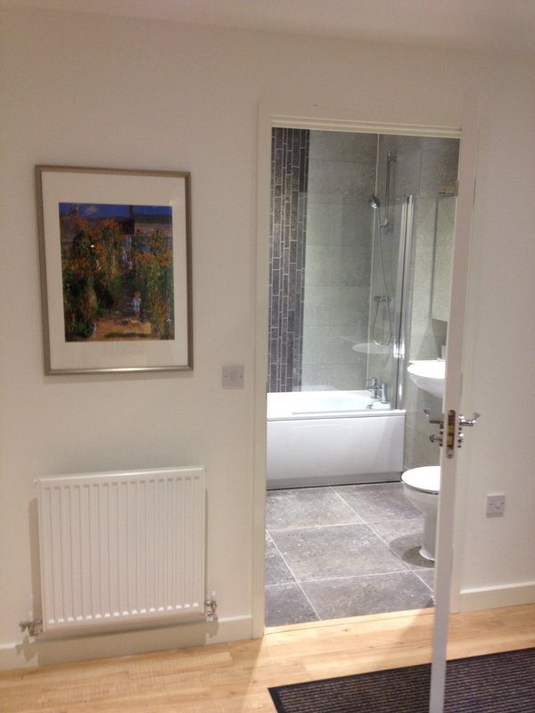 Hallway with wooden floor, white radiator, framed artwork, and open door to modern bathroom