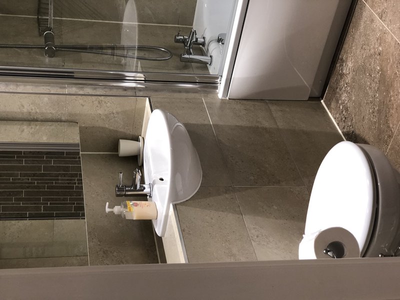 Modern bathroom with two white toilets, grey tile flooring, shower area and vanity sink