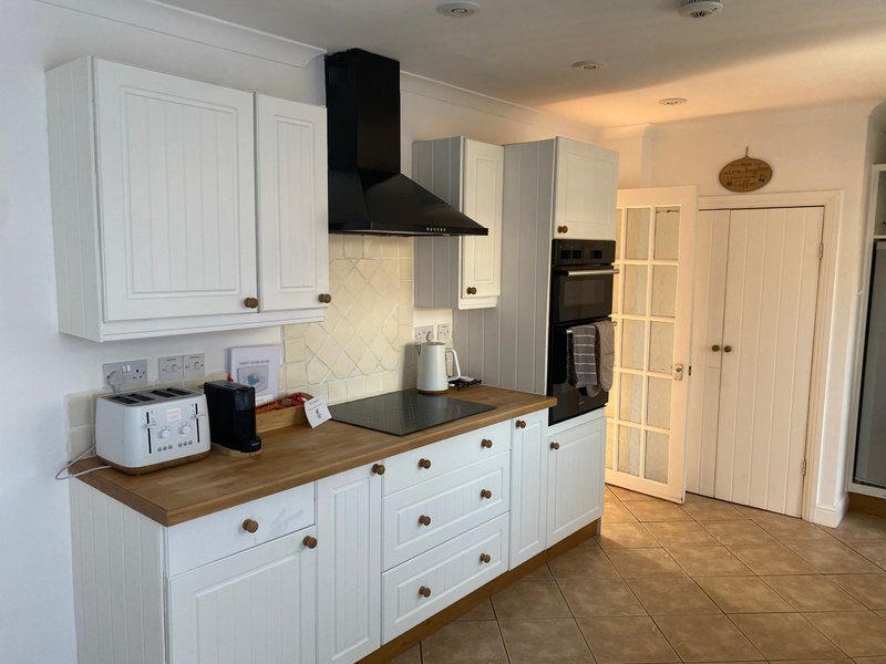 Modern kitchen with white cabinetry, wood countertop, black cooker hood and cream tile backsplash