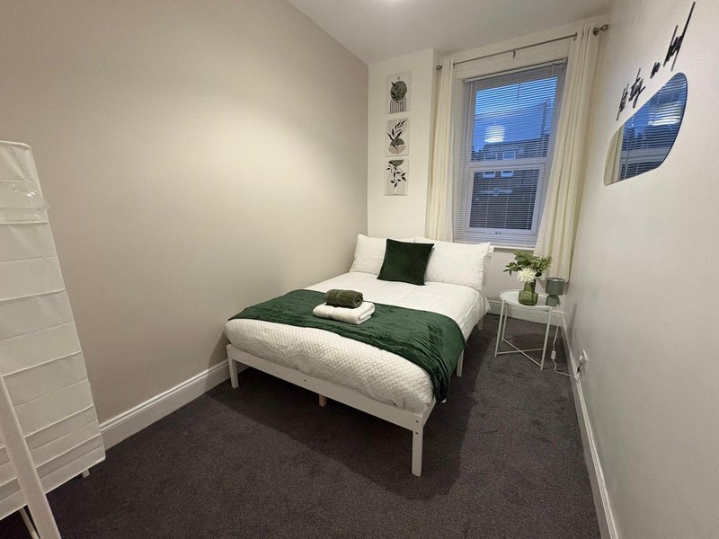 Compact bedroom with single bed, green bedding, white pillows, small side table and window