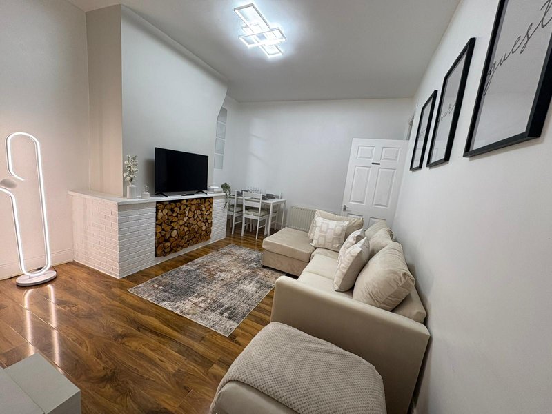 Modern living room with beige seating, wooden floor, TV unit, and wall art
