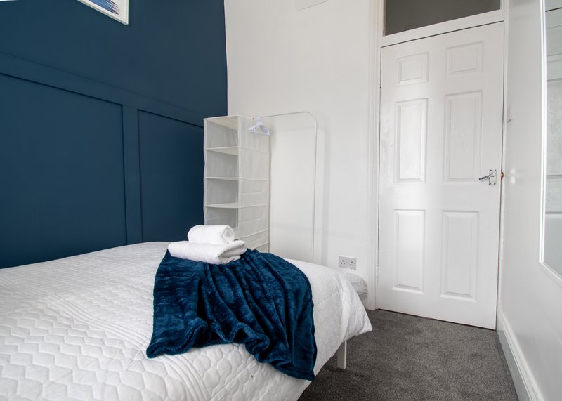 Modern bedroom with single bed, white bedding, navy throw, and dark blue accent wall