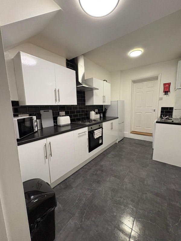 Modern kitchen with white cabinets, black backtile, dark flooring and integrated appliances