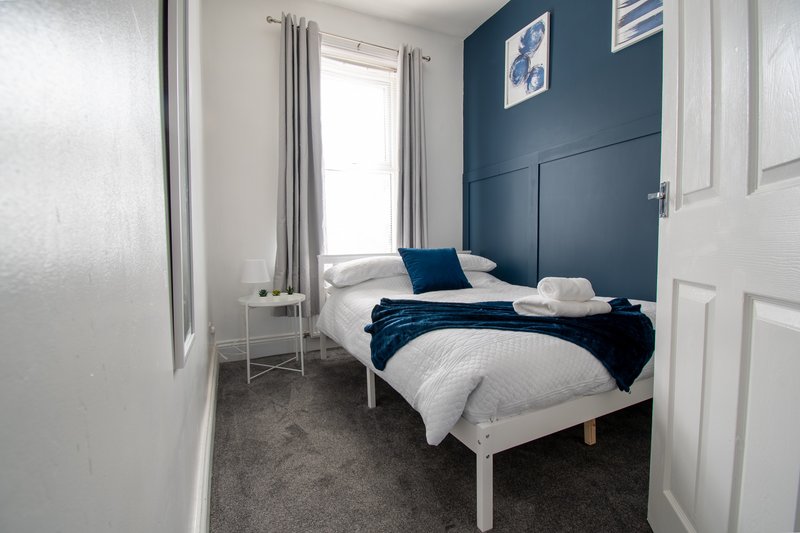 Small bedroom with single bed, navy blue feature wall, white bedding and window with curtains