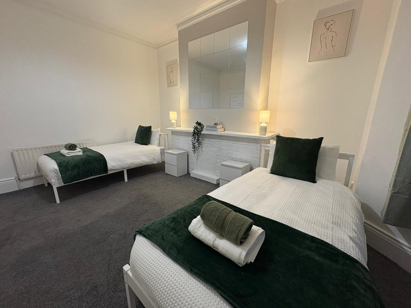 Bright twin bedroom with two beds, shared vanity mirror, wall art, and green cushions