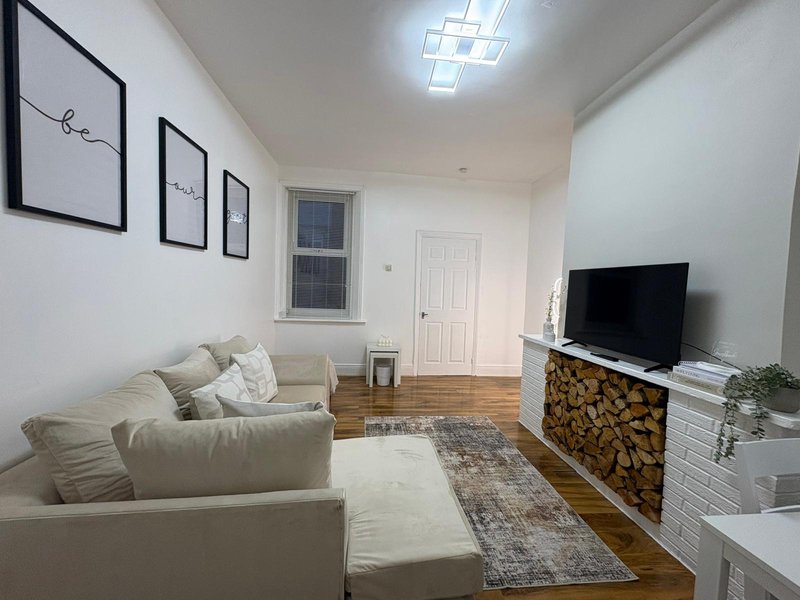 Bright living room with cream sofa, TV on fireplace mantel, wooden floors and framed wall art