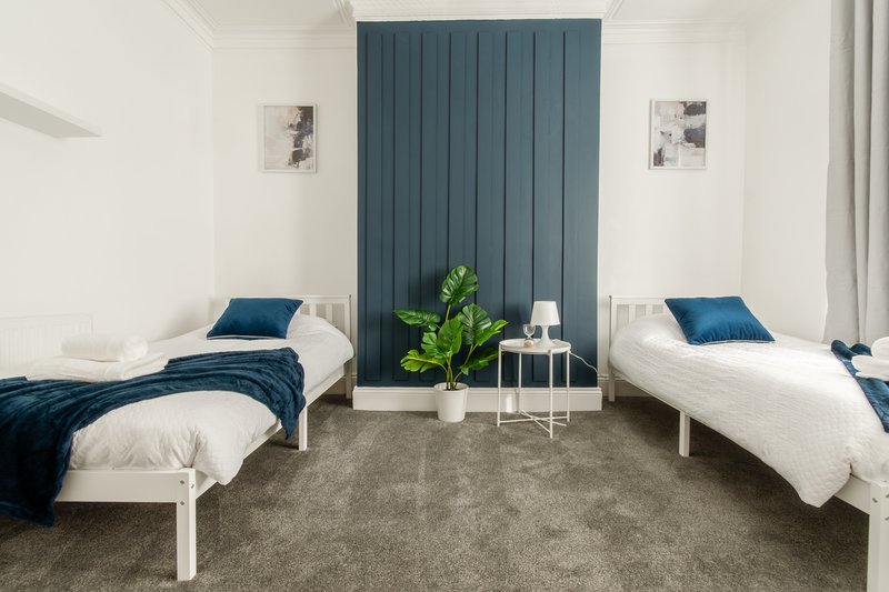 Twin bedroom with two white beds, blue bedding, teal accent wall, potted plant and white side table