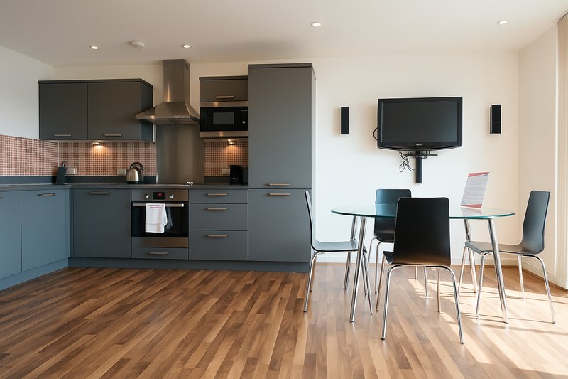 Open-plan kitchen and dining area with blue cabinetry, dining table, and wall-mounted television