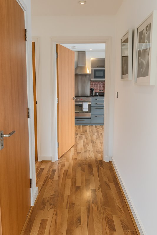 Hallway with wooden doors, wood flooring, leading to kitchen with blue cabinetry