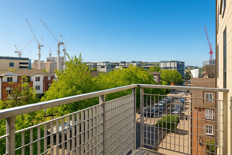 Balcony with metal railing overlooking urban neighborhood with construction cranes and green trees