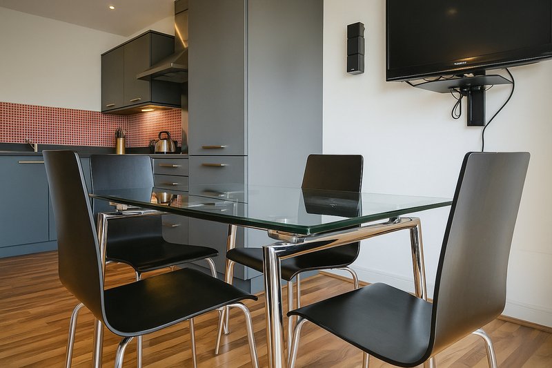 Modern open-plan kitchen and dining area with glass table, black chairs, and wall-mounted TV
