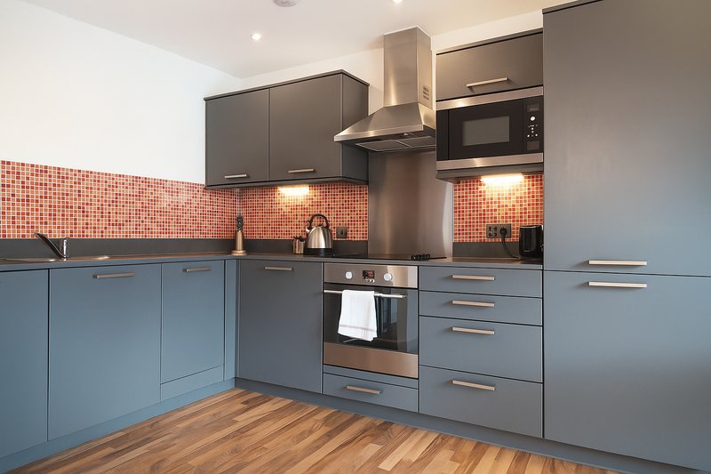 Modern kitchen with blue cabinetry, orange tile backsplash, stainless steel appliances and wooden flooring