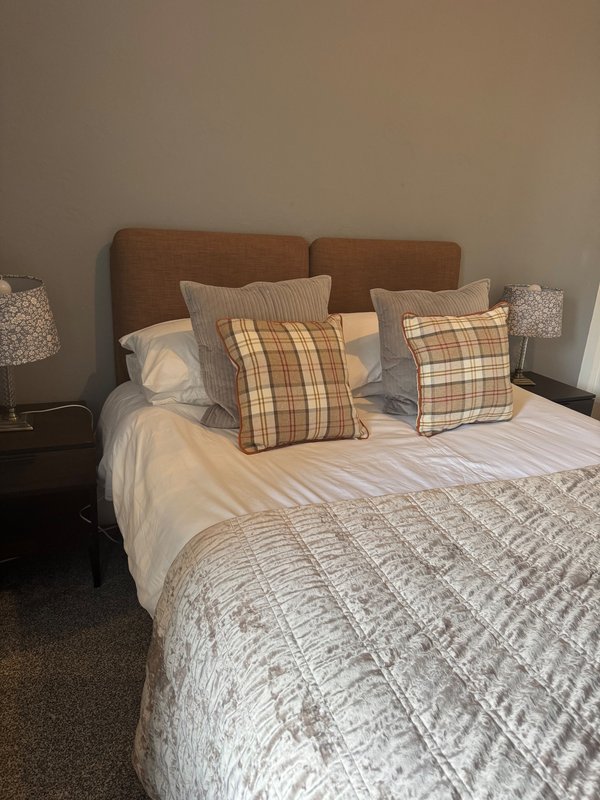Bedroom with brown upholstered headboard, double bed, patterned cushions and bedside lamps