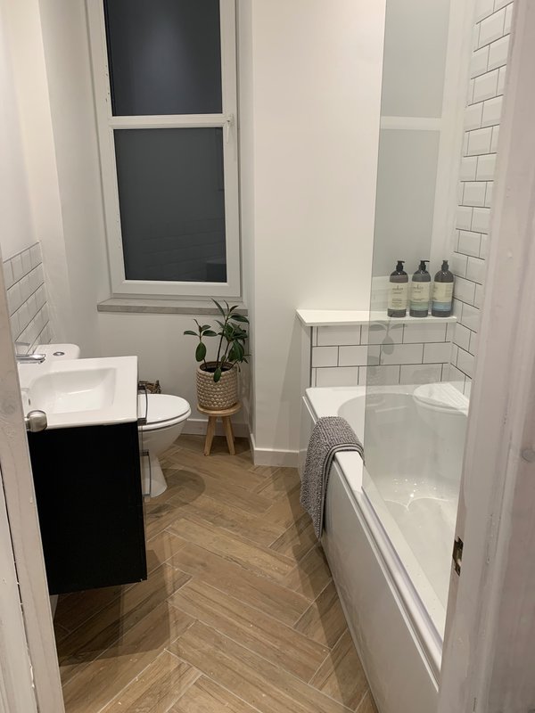 Modern bathroom with toilet, bathtub, white subway tile, wooden floor and window