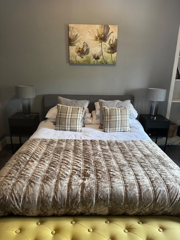 Modern bedroom with double bed, patterned bedding, plaid cushions, bedside tables and botanical wall art