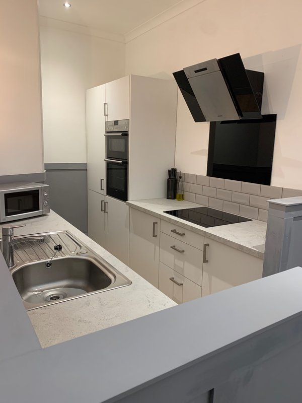 Modern galley kitchen with white cabinetry, stainless steel sink, induction cooktop, and black range hood