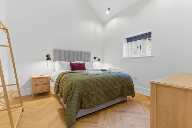 Bright bedroom with double bed, grey headboard, wooden nightstands and herringbone flooring