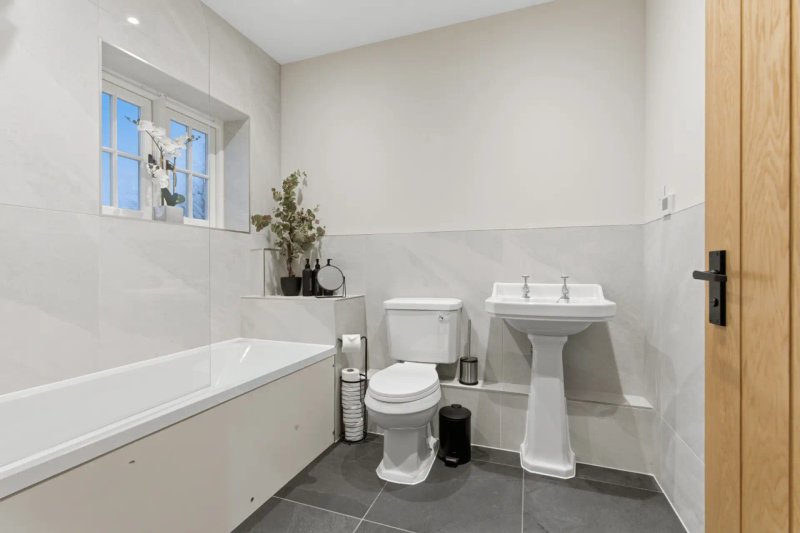 Modern bathroom with bathtub, pedestal sink, toilet, and window with natural light