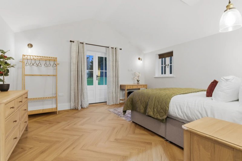 Spacious bedroom with two beds, wooden furniture, herringbone flooring and glass doors