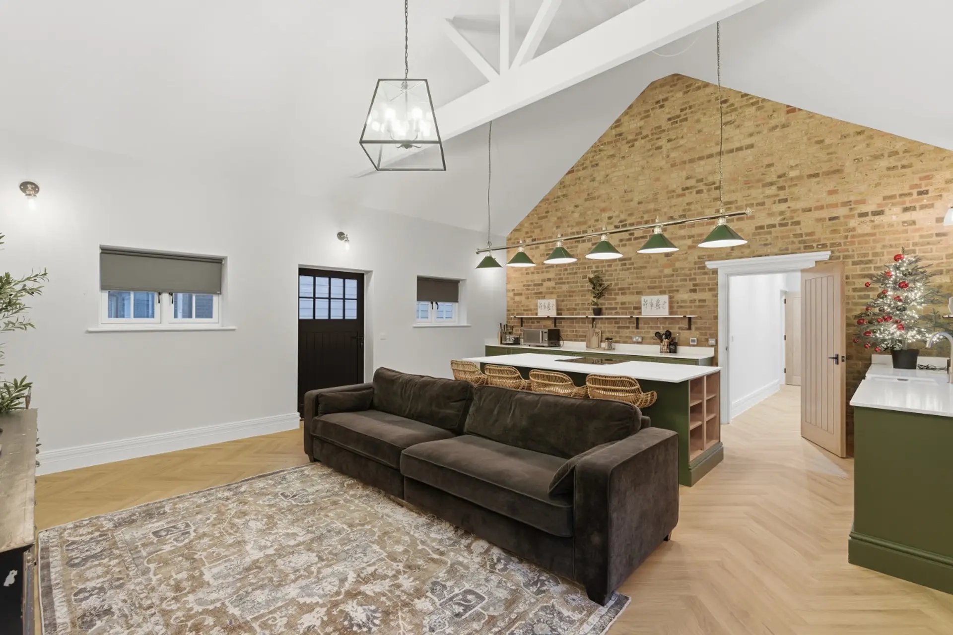 Open-plan living space with dark sofa, kitchen island, exposed brick wall and pendant lighting