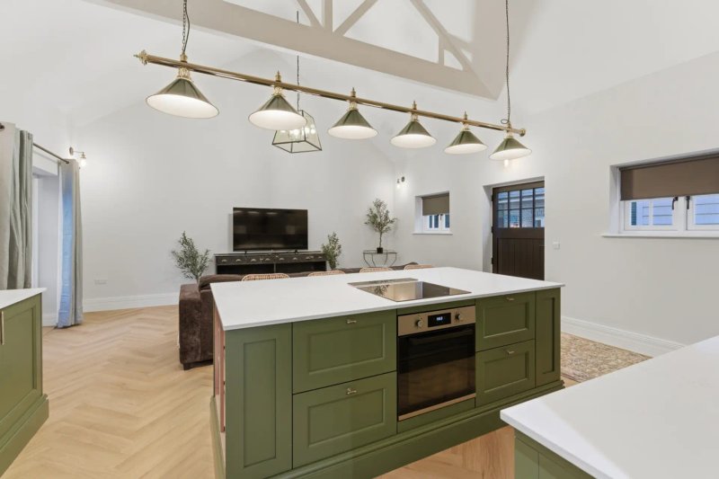 Modern open-plan kitchen and living area with green island, pendant lights, wooden floor and fireplace